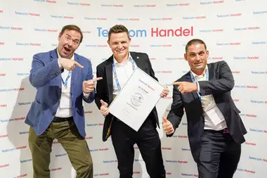 Drei Männer in Anzügen präsentieren stolz eine Auszeichnung auf einer Konferenz.