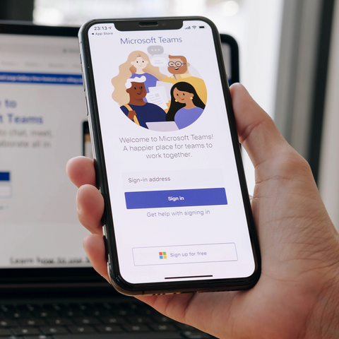 Handy in einer Handy, iPad auf dem Tisch, Microsoft Teams Log-in wird angezeigt